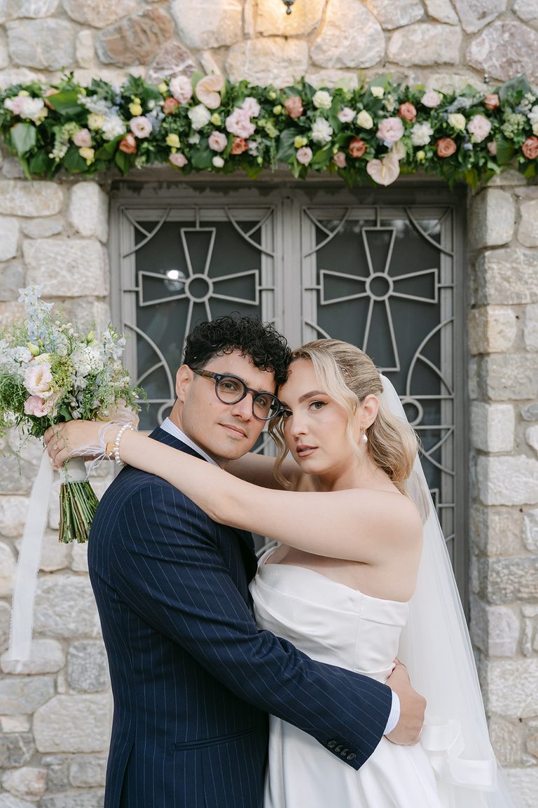 George & Nafsika, wedding in Aigio: an embrace at the chapel door with its flower garland